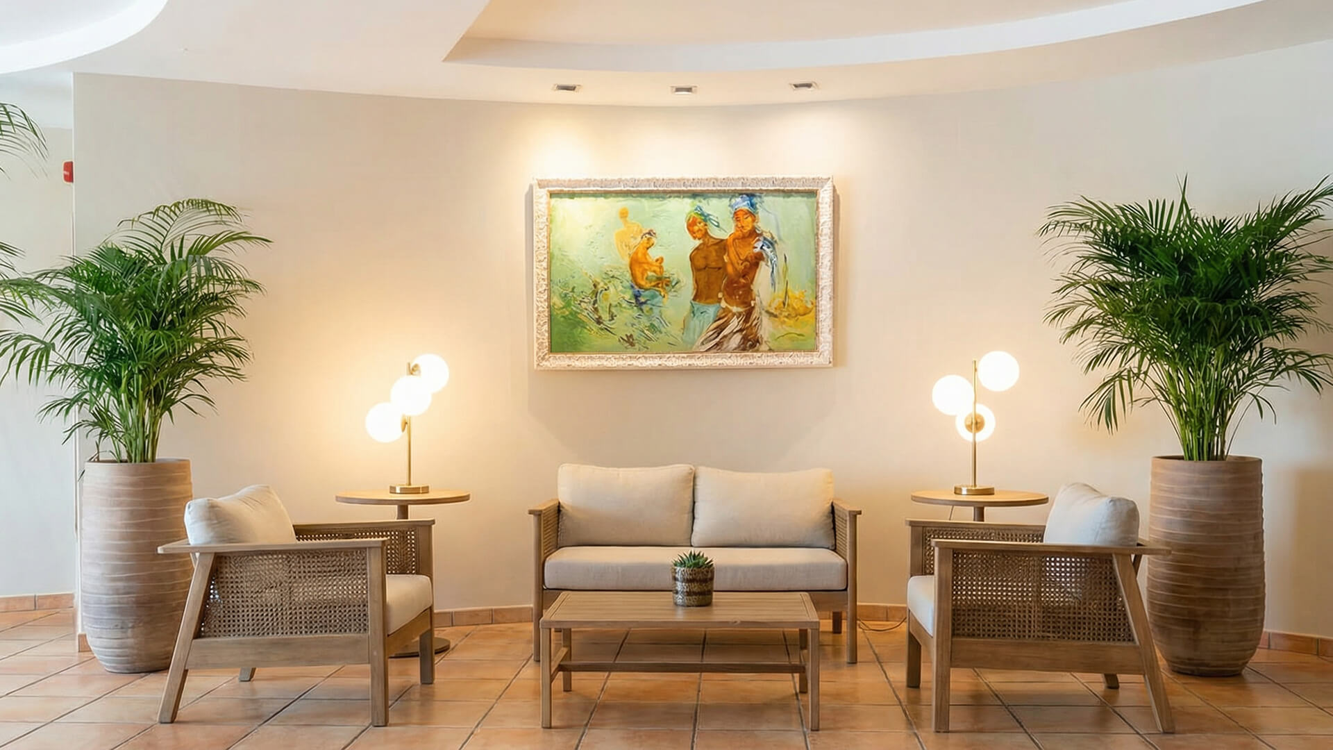Una zona de estar con un sofá beige, dos sillones, una mesa de centro, dos plantas en macetas y un cuadro en la pared de arriba, iluminado por dos lámparas de pie.